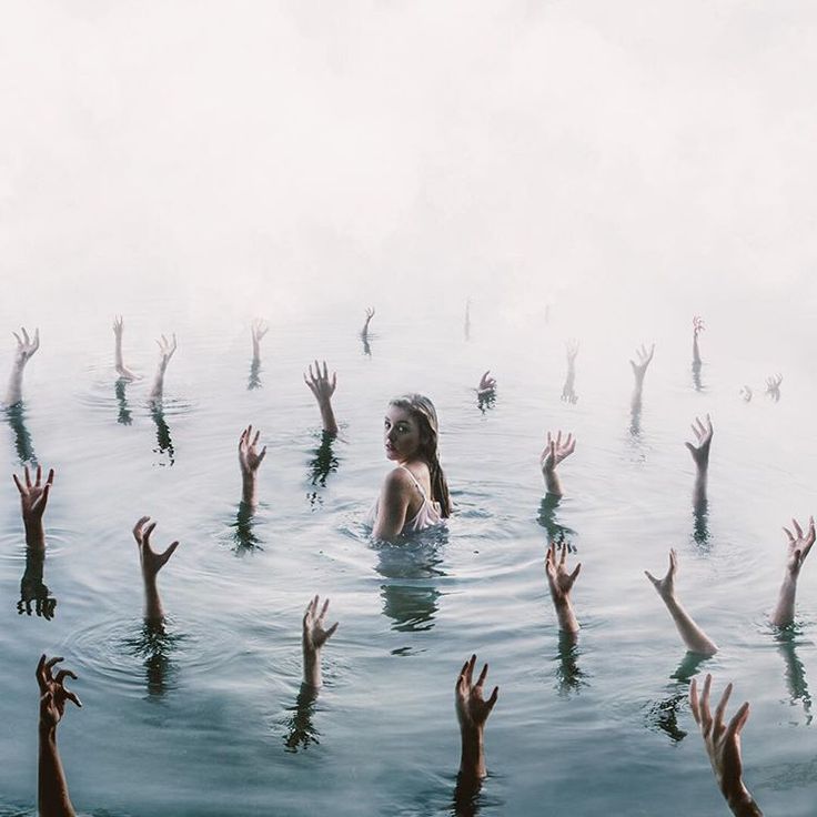 a young woman is waistdeep in water, surrounded by numerous arms and hands reaching upwards from below the surface. the water is calm but slightly disturbed by the hands. a dense fog hangs in the air above the water. the image has a surreal and ominous atmosphere. the woman looks over her shoulder with an intense expression.