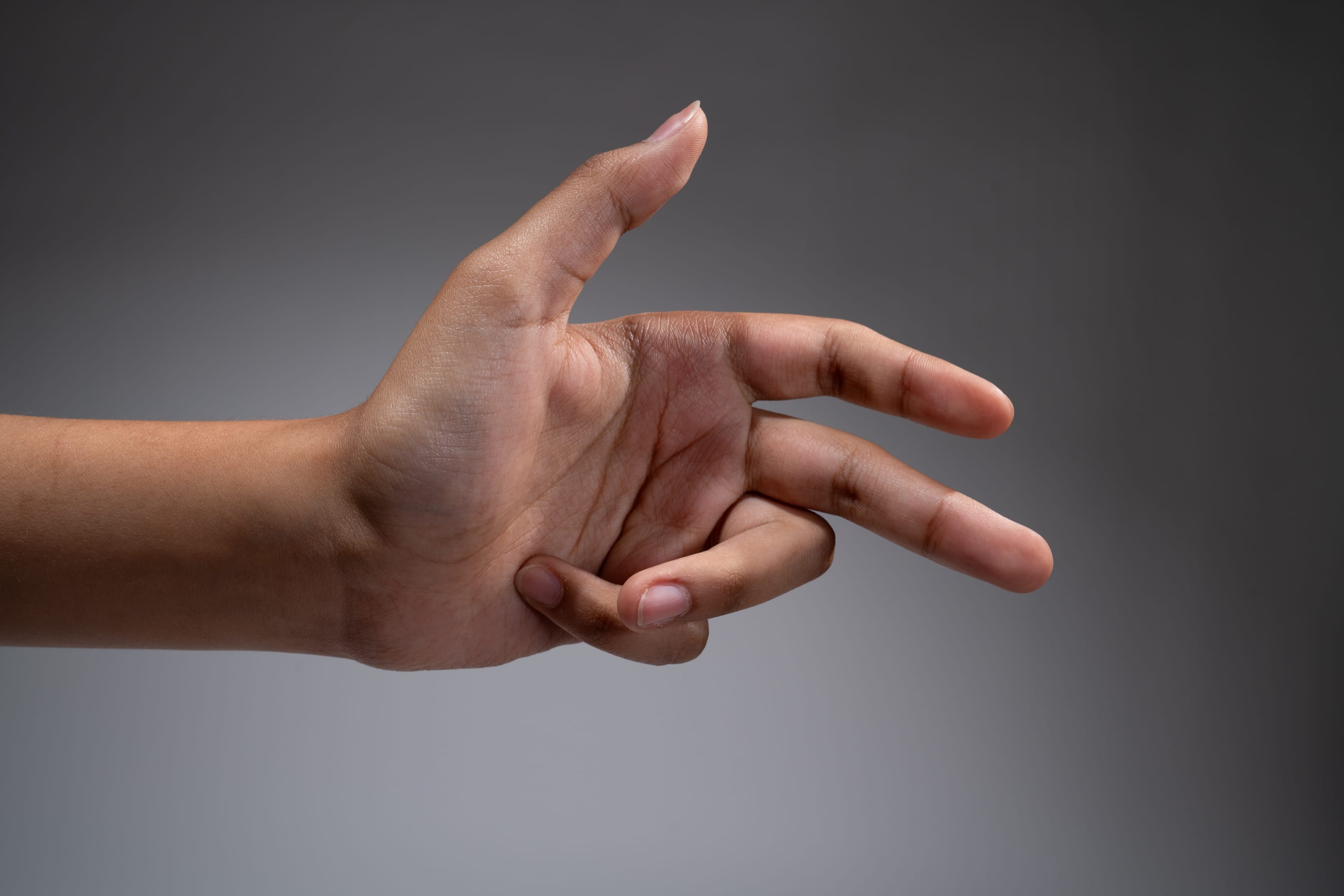 a hand is held up against a gray background with the thumb, index, and middle finger extended and the other fingers curled into the palm.