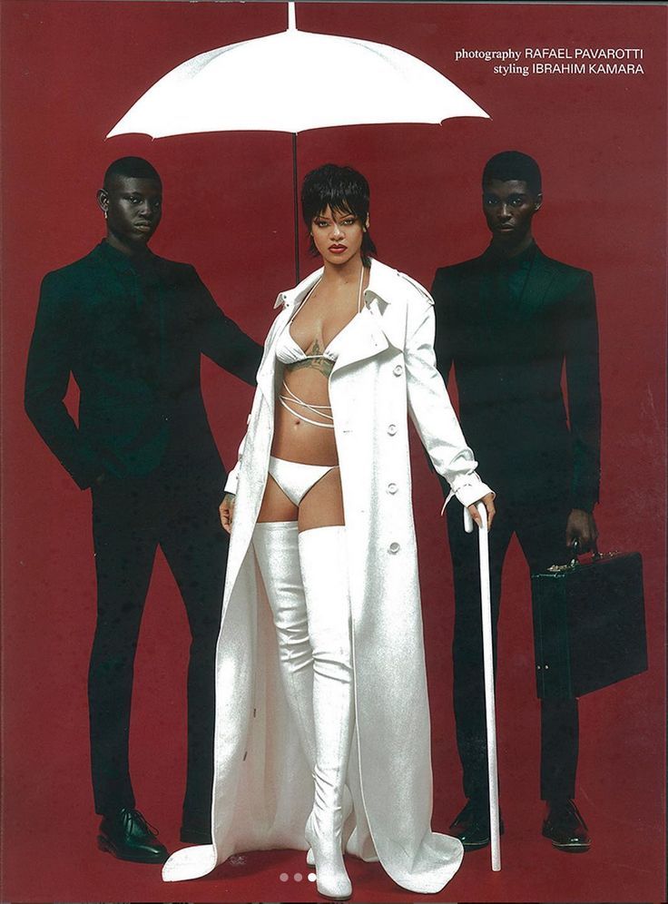 rihanna is the center of attention, wearing a white coat, boots, and lingerie. she is posed with her hands on a walking stick and her head slightly tilted. two men stand on either side of her, both dressed in black suits. they have serious expressions on their faces. the background is a solid red color. the image is likely from a photoshoot for a magazine.