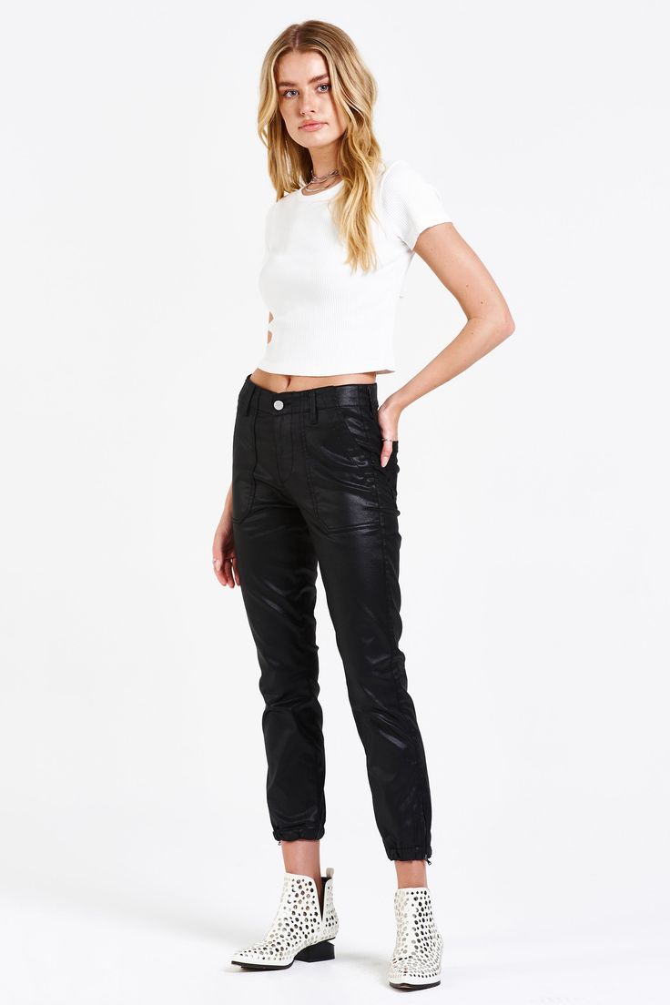 a fullbody shot of a model wearing a white cropped ribbed top and black coated joggerstyle pants. she is also wearing white studded ankle boots.  the background is white. the image is a studio shot.
