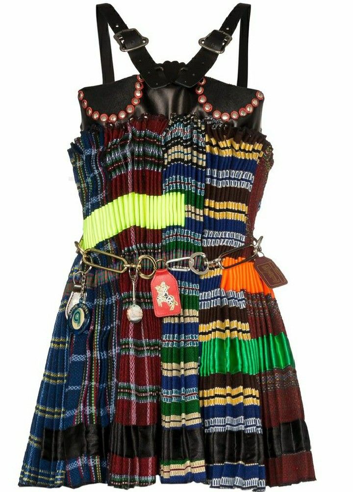 loseup view of a women's multicolored mini dress. the dress features a patchwork design with various plaid and tartan patterns in bright colors.  it has a pleated skirt and a bodice with black leather straps and studded details. a gold chain belt with several charms is fastened around the waist. the overall style is eclectic, quirky and highfashion.