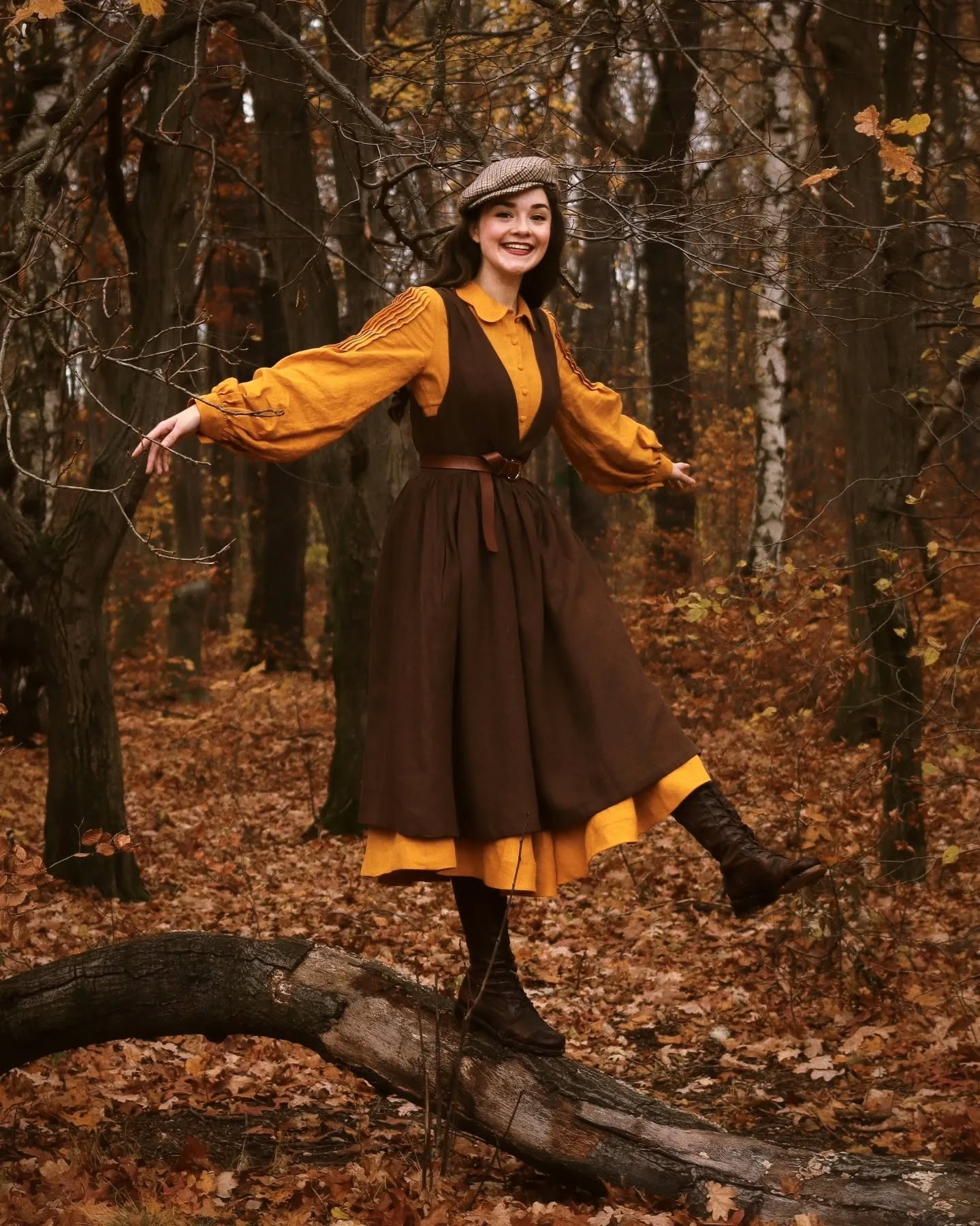 a young woman, smiling brightly, balances on a fallen log in an autumnal forest. she's wearing a stylish vintageinspired outfit: a brown pinafore dress over a mustardyellow longsleeved blouse, brown boots, and a newsboy cap.  the forest floor is covered in a carpet of fallen goldenbrown leaves, adding to the overall autumnal ambiance. the scene is captured with a warm, slightly muted color palette, creating a whimsical and nostalgic atmosphere. the woman's pose and joyful expression enhance the charming and romantic feeling of the image.