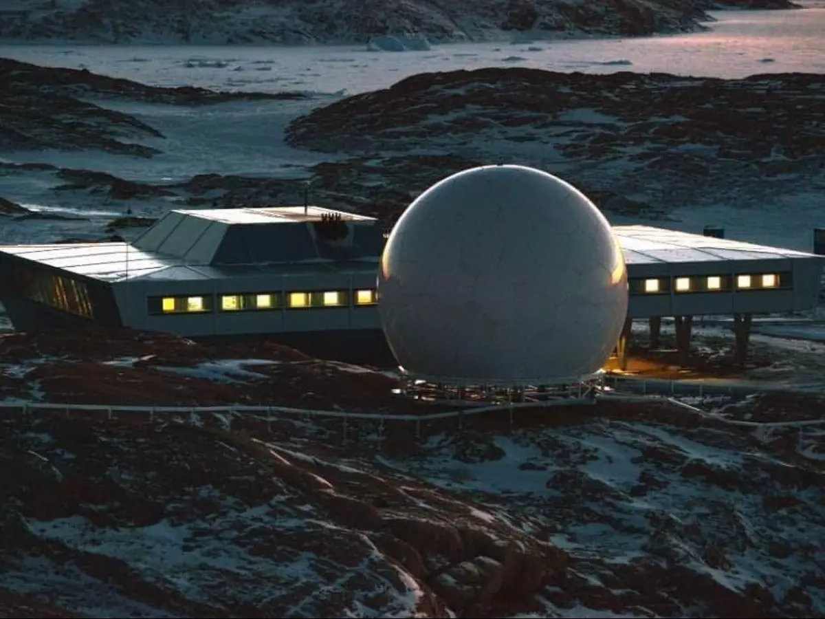 a large, spherical radar antenna stands in the arctic or antarctic, surrounded by snow and ice. a building stands beside the antenna, and it is possibly a research station. the scene is desolate and cold, but the antenna is a testament to the power of technology.