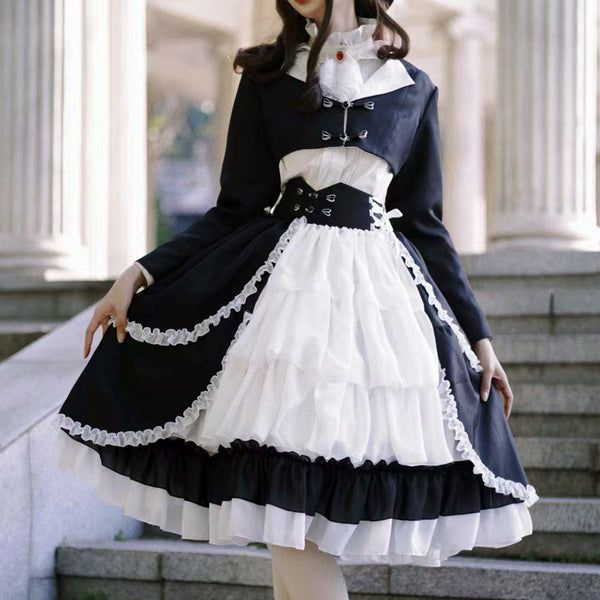 a young woman in an elegant black and white lolita fashion dress poses on a set of stairs in front of a grand building. her outfit features a black bolero jacket over a white blouse with a large statement collar, and a black and white tiered skirt with lace and frill detailing. the overall aesthetic is sophisticated and stylish.
