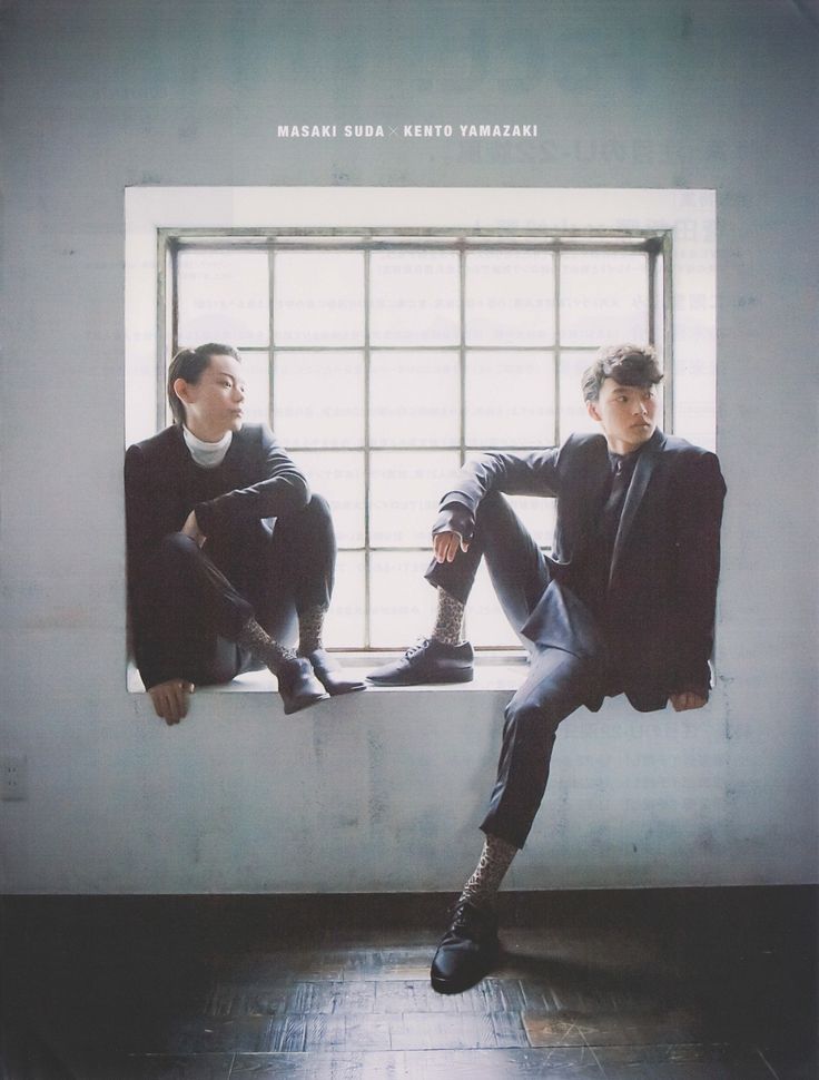 two men in black suits are sitting on a ledge in front of a large window. the man on the left is masaki suda, and the man on the right is kento yamazaki. they are both looking to the right of the frame. the image has a soft lighting and an eye level perspective.
