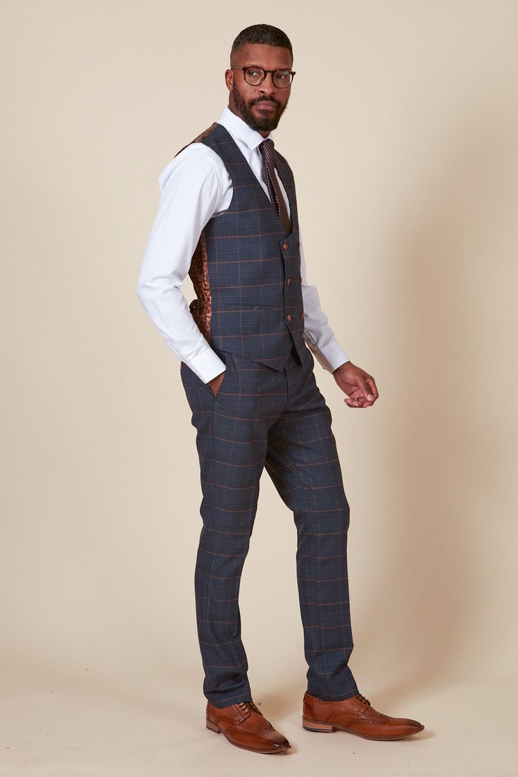 a fulllength studio shot of a man modeling a navy blue checkered suit with an orange check pattern. he's wearing a matching waistcoat, a white shirt, and a brown tie. the man is wearing brown leather shoes and eyeglasses. he has a short, wellgroomed haircut and beard. the background is a light beige color.  the overall style is formal and sophisticated.