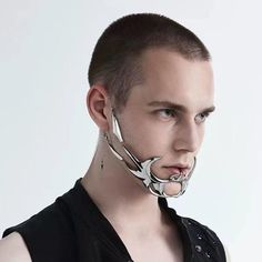 a closeup portrait of a young man with short hair modeling a silver, metallic jaw and ear cuff.  the jewelry piece is intricate and angular, evoking a cyberpunk or futuristic aesthetic. the image is shot against a white background with soft lighting, highlighting the details of the accessory.