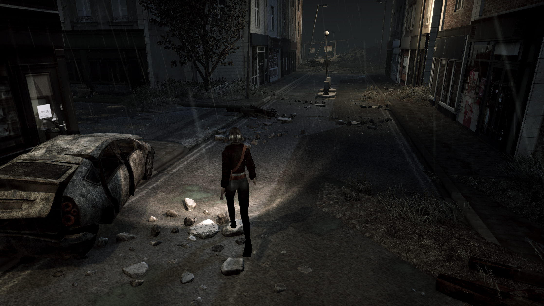 the image shows a woman walking down a deserted, rubblestrewn street at night. the street is lined with buildings, some of which are damaged. there is a wrecked car on the left side of the street and a downed tree on the right. the street is lit by a streetlight and the woman is holding a flashlight. it is raining.
