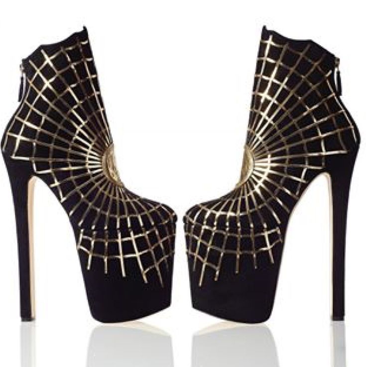 a pair of black, highheeled ankle boots with a gold spiderweb design. the shoes have a stiletto heel and a platform sole, giving them a very high and fashionable look. they are sitting on a reflective surface, suggesting they are in a studio or retail setting.