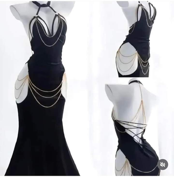 the image shows a black lingerie dress with gold chains attached to the straps and around the waist.  the dress is being worn by a female model in a studio setting. the image is likely taken for an online store or fashion magazine. the image is focused on the dress, emphasizing the details and design. the model's pose and expression are