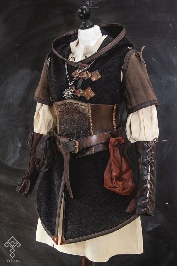 a mannequin displays a costume reminiscent of something from the witcher universe. the outfit consists of a hooded tunic in black with brown leather detailing, cinched at the waist with a wide, tooled leather belt. leather gauntlets with laceup details and a pouch hang at the sides. a necklace with a wolf medallion completes the ensemble.