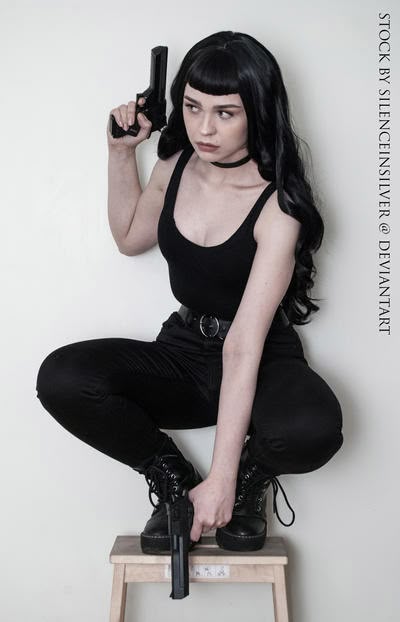 a woman with black hair is squatting on a stool while holding a gun. she is wearing a black tank top, black pants, black boots, and a choker. the background is white.