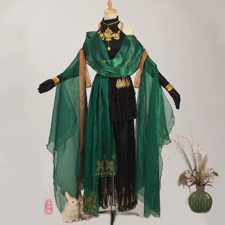 this is a photo of a mannequin wearing a beautiful and elaborate green dress. the dress is long and flowing, with long sleeves, and gold accents and jewelry. it appears to be made of a shimmering green fabric. the mannequin is also wearing black pants and gold jewelry.  a white rabbit is on the floor next to the mannequin.  the background is white, and there is a vase of white flowers on the right side of the image.