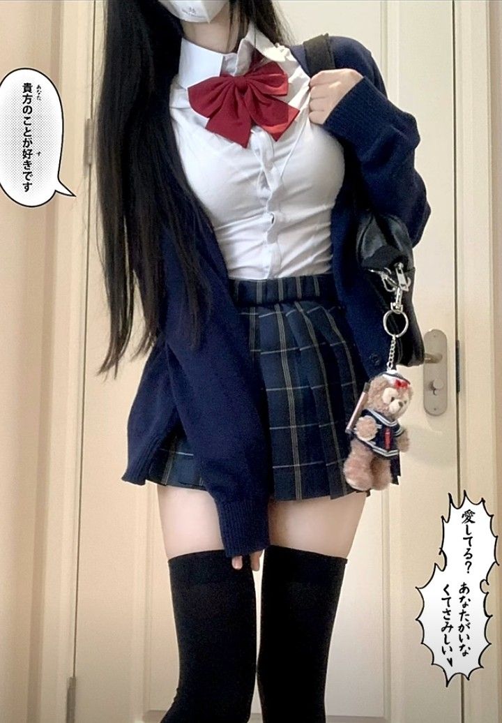 a young woman is dressed in a japanese school girl uniform, which includes a white shirt with a red bow tie, a navy blue cardigan, a pleated plaid skirt, and black kneehigh socks. she is holding a black handbag with a teddy bear keychain attached. the background is a lightcolored wall. japanese text is present in speech bubbles.