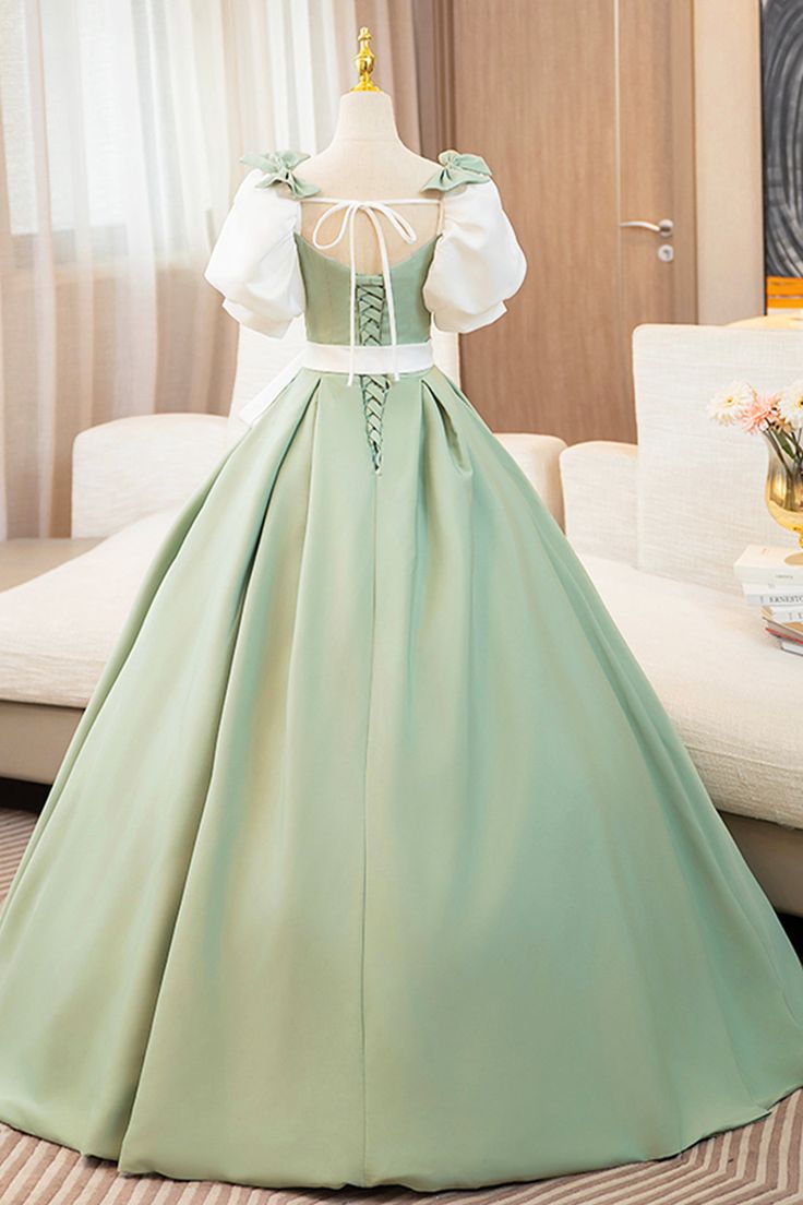 a back view of a sage green satin ball gown displayed on a mannequin. the gown features a corset back with laceup details,  offtheshoulder puff sleeves in white, and a flowing aline skirt. the dress is showcased against a clean white background in a studio setting with soft, natural lighting.