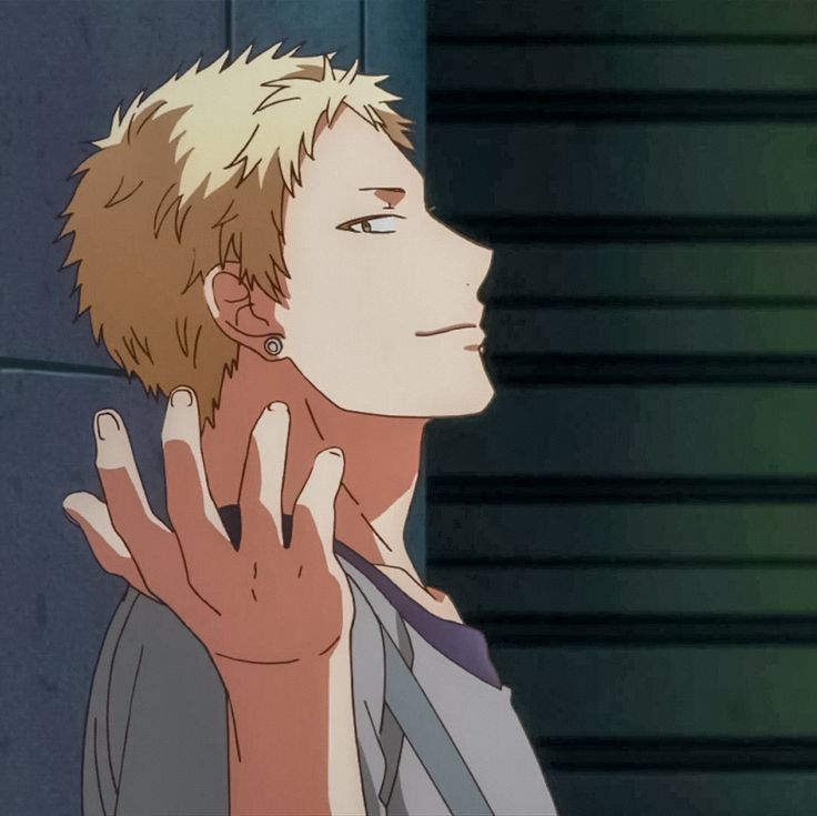 this image features a young male anime character with blond hair, he has a piercing in his left ear, and is wearing a grey shirt. he is standing in a street, with his back to the wall and his right hand raised. the background is a blurry depiction of a wall and a street, with some shadows.