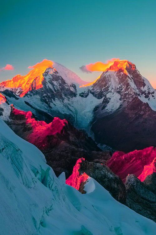 a breathtaking panoramic view of a snowcapped mountain range bathed in the warm glow of a vibrant sunset. the peaks are illuminated in a dazzling array of colors, with orange and pink hues dominating the highest points, while the valleys below are cast in a deep blue shadow. the clouds above are painted in shades of orange and red, adding to the dramatic beauty of the scene. the pristine snow and ice cover the landscape, creating a sense of tranquility and awe. the rugged mountains and the vastness of the scene inspire a sense of wonder and adventure. this image captures the essence of a truly unforgettable natural spectacle.