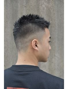 a side view of an asian man with short, spiky hair styled in a fade haircut. he is wearing a black tshirt and the background is a textured gray wall.