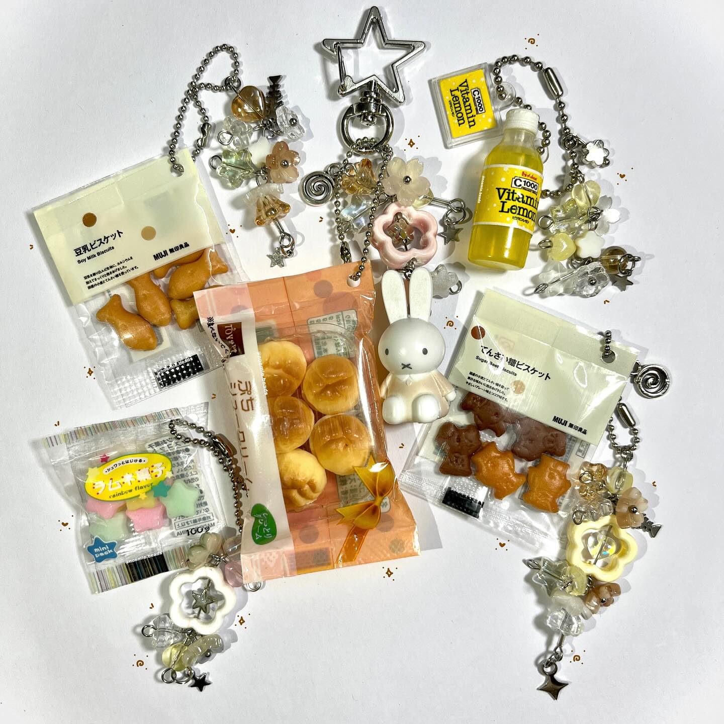 the image shows a collection of keychains featuring miniature versions of food items and novelty characters. the keychains include miniature bags of biscuits with shapes of fish and animals, small packs of candies, tiny cream puffs, a miffy rabbit figurine, and a miniature vitamin c drink bottle, along with decorative elements like beads, flowers, and star charms, all attached to silver chains and keyrings.