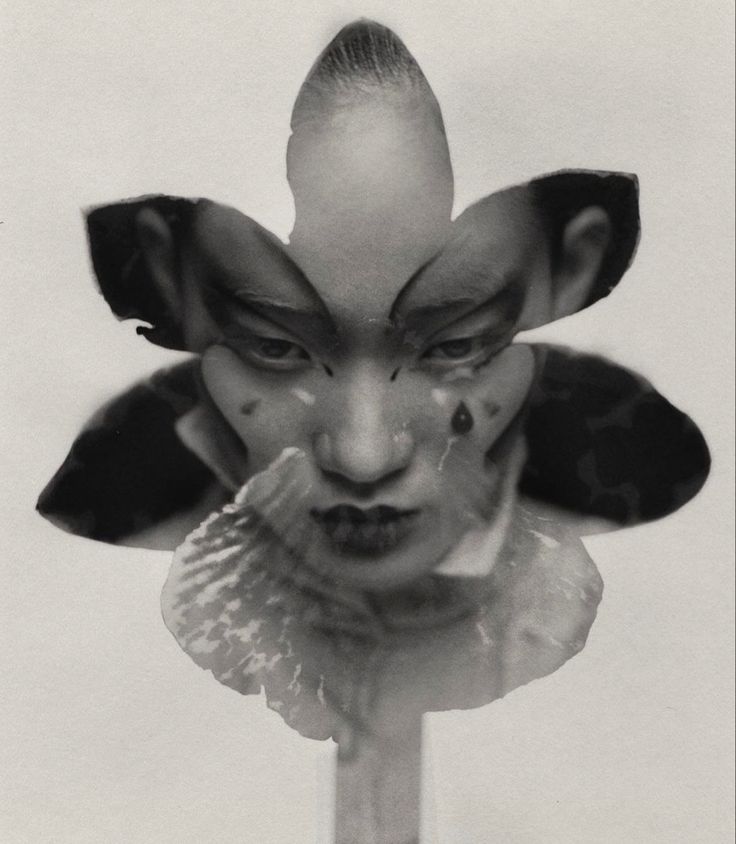 the image is a striking black and white portrait of a woman's face.  her face is partially obscured and overlaid with what appears to be a stylized flower, possibly a lily or orchid. the woman wears dramatic clownlike makeup, with exaggerated features and streaks that resemble tears running down her cheeks. the contrast between the delicate flower and the intense makeup creates a surreal and unsettling atmosphere. the overall style is artistic and darkly expressive, potentially falling within the genres of fashion or fine art photography. the image's texture and use of light and shadow add depth and complexity.