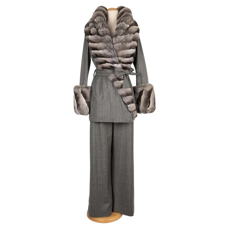 a fulllength shot of a women's grey pinstriped suit with a wideleg pant, a collared jacket and fur trim on the collar and cuffs. the suit is belted at the waist and is shown on a mannequin.  the suit looks vintage.  the mannequin is on a white background.