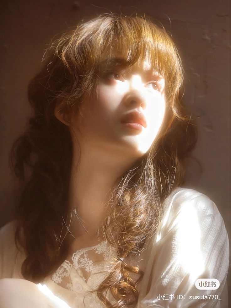 a portrait of a young woman with brown hair and bangs, bathed in sunlight. she is wearing a white lace top.