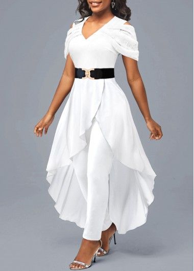 a woman is posing in a white sleeveless dress that has a high waist with a black belt. she is wearing white pants and high heels. she is standing in front of a plain white background and looking at the camera.