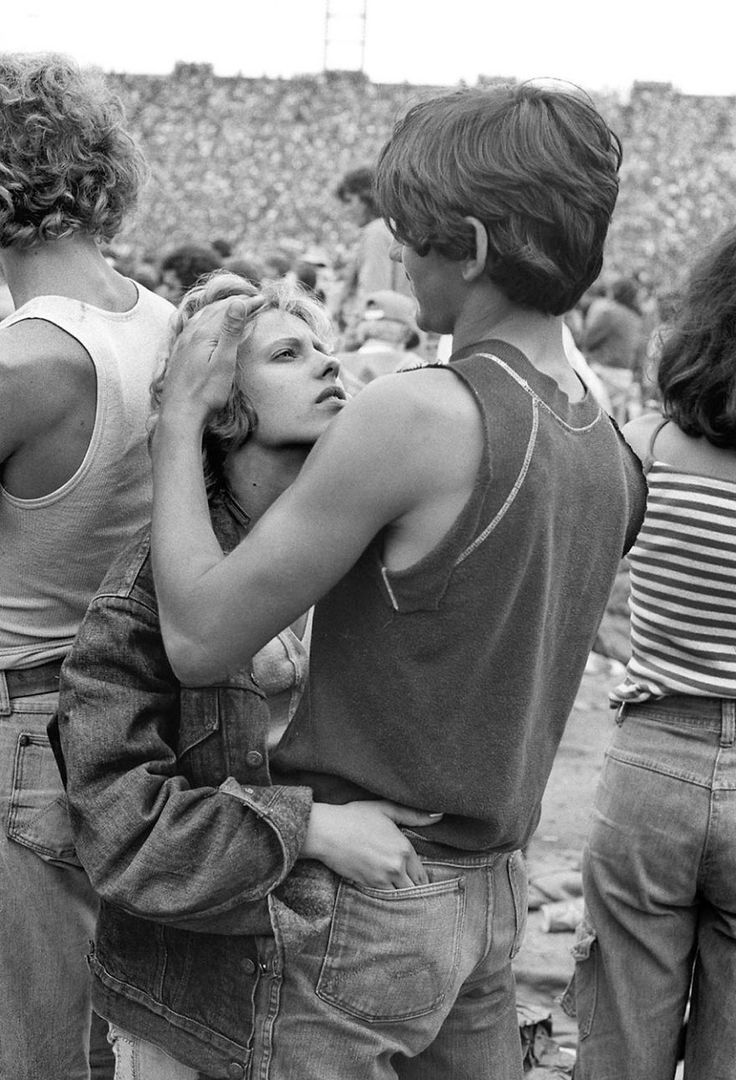 a young couple stands in the middle of a large crowd, looking at each other.