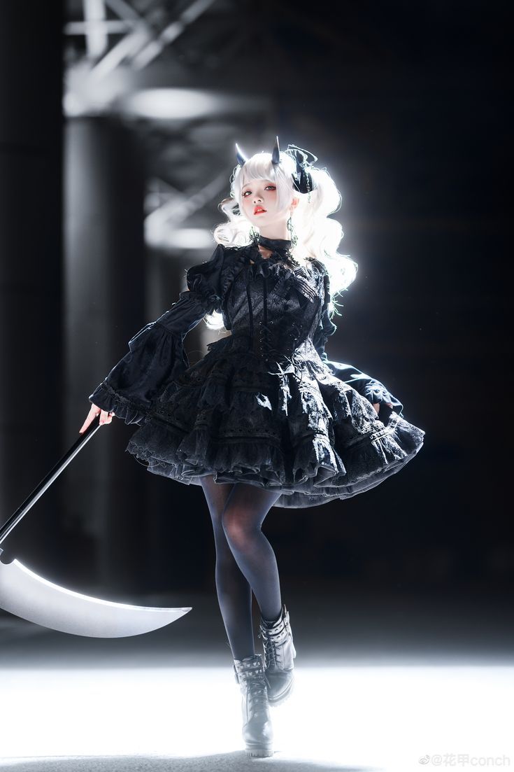 a young woman with white hair, wearing a black gothic dress and horns, poses with a large silver scythe in a studio setting.
