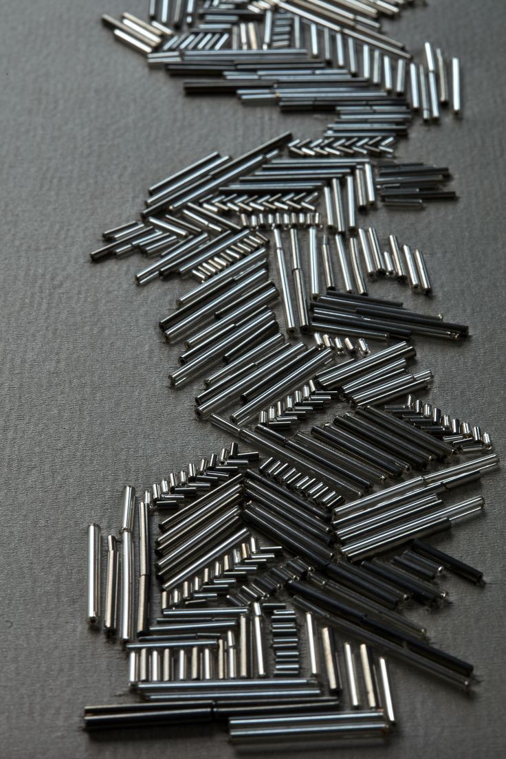 the image shows a closeup of a collection of small, metallic rods or cylinders arranged in a geometric pattern on a gray background. the rods are silver in color and vary in length, creating a textured and visually interesting composition.