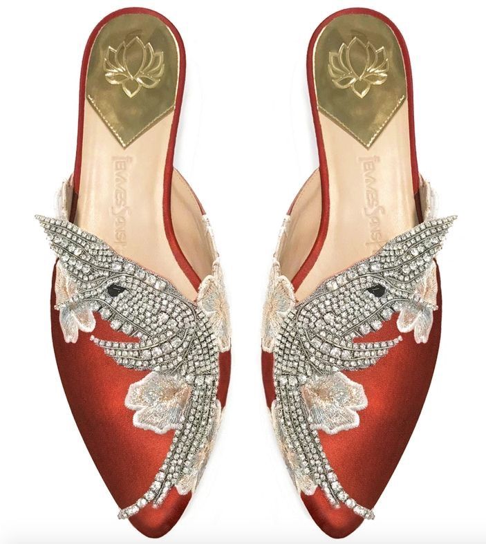 a pair of red emre sayasci mules with pointed toes are shown from a topdown perspective. the shoes are embellished with crystals and floral embroidery, and feature a gold lotus design on the insole. the mules have a red trim around the opening.