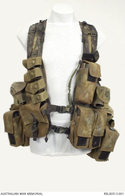 a closeup of a military vest with various pouches and straps. the vest is made of camouflage fabric and has a worn and weathered appearance.  the vest is equipped with a variety of pouches and straps, including a large pouch on the front, two smaller pouches on the sides, and a number of straps for attaching additional gear.  the vest is a key piece of equipment for soldiers in combat, as it allows them to carry a variety of essential supplies and gear.
