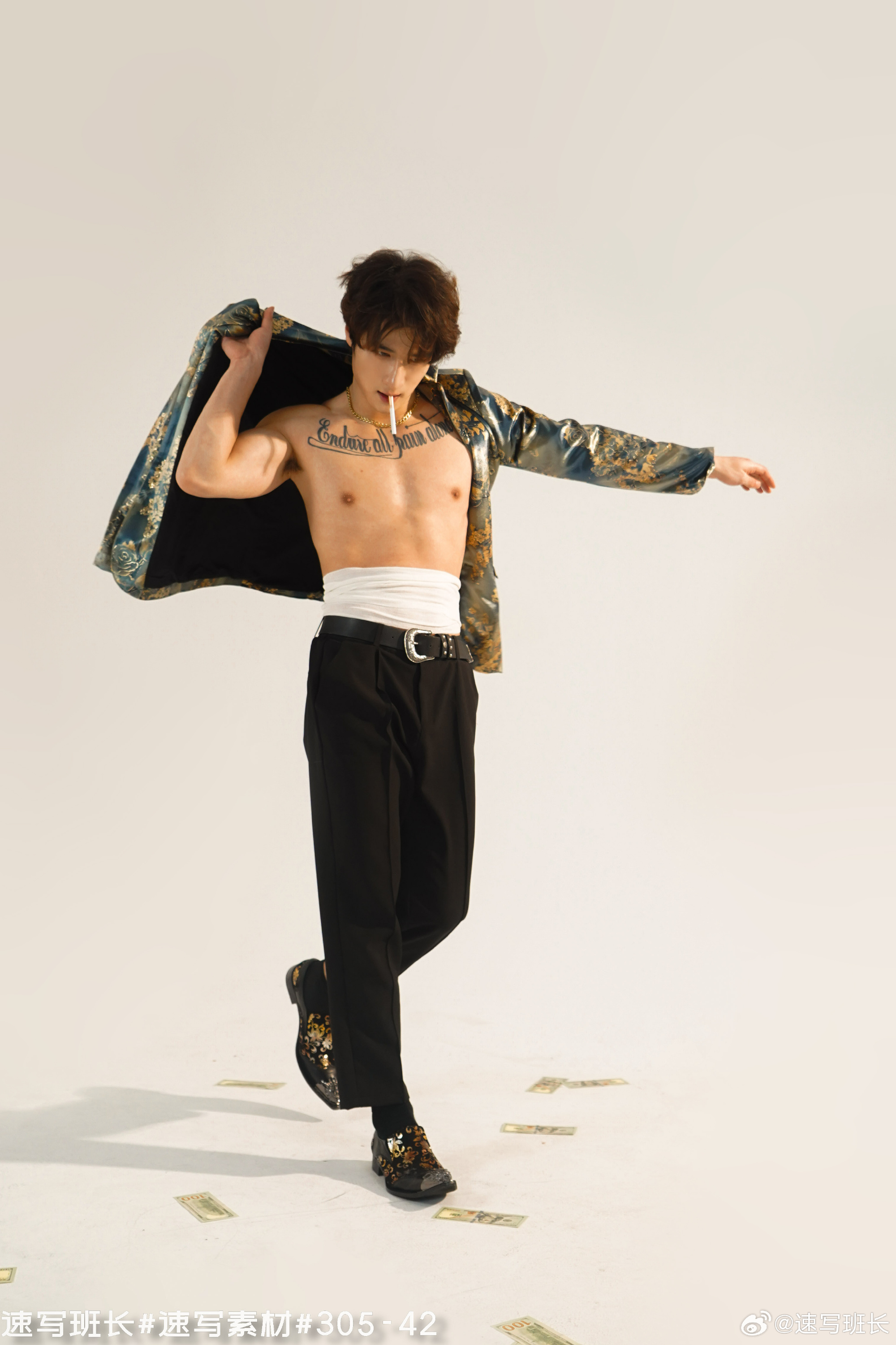 a man with tattoos and a cigarette is posing on a white background. he is wearing black pants with a white belt, and a blue and gold jacket that he's holding open. his chest is bare and he has a cigarette in his right hand. he is stepping on scattered paper money.
