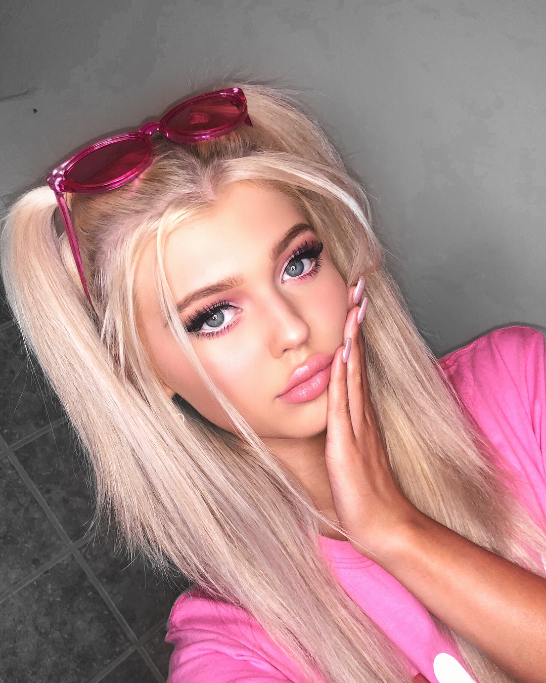 a selfie of loren gray with blonde hair in pigtails, wearing pink sunglasses and a pink shirt, with prominent makeup and lightcolored eyes.