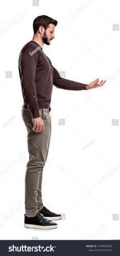a young adult man with a beard and short brown hair is standing against a white background in a studio. he is wearing a brown sweater, green pants, and black sneakers. he is reaching out with his right hand.