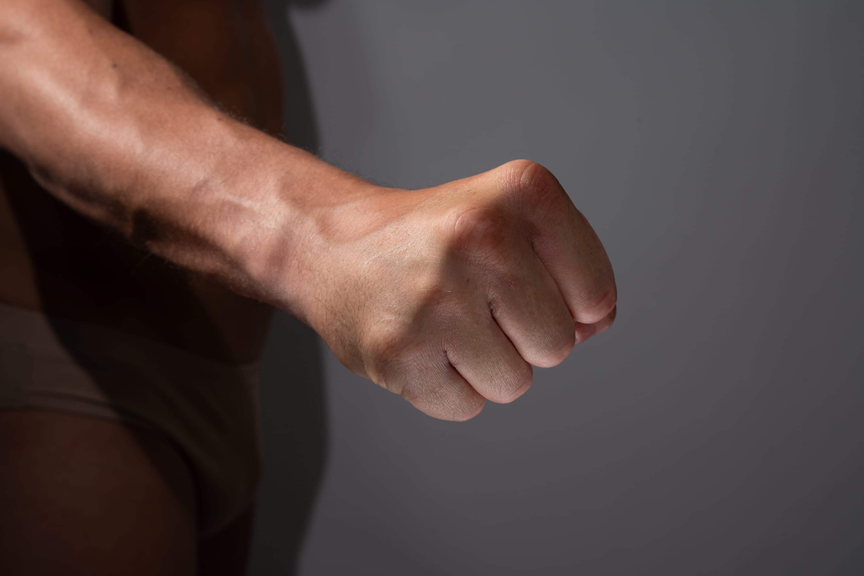 the image shows a closeup of a man's clenched fist. the fist is illuminated by studio lighting, casting a shadow on the background. the image conveys a sense of strength and power.