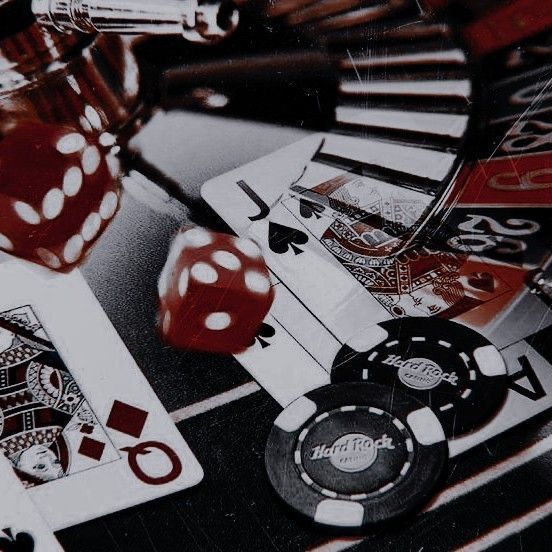 the image showcases a closeup view of a casino table, scattered with various gambling paraphernalia. two sixsided dice, blurred due to motion, take center stage, one red and one black with white dots. several playing cards are strewn around, some facedown, others revealing the ace of spades, jack of spades, and queen of diamonds. two hard rock cafe poker chips complete the scene, one partially obscuring the other, both boasting a black background with white and red detailing. the table beneath is a dark, nondescript surface, adding to the overall ambiance of a highstakes game in progress. the dim lighting casts subtle shadows, enhancing the sense of clandestine excitement and anticipation.