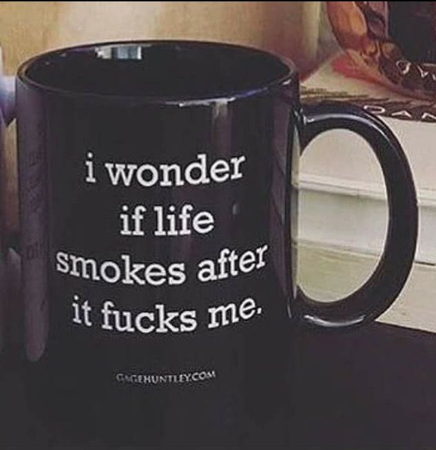 a black mug is sitting on a table with a stack of books in the background. the mug has white text printed on it that reads, "i wonder if life smokes after it fucks me". the website "gagehuntley.com" is printed in smaller text below the main text.