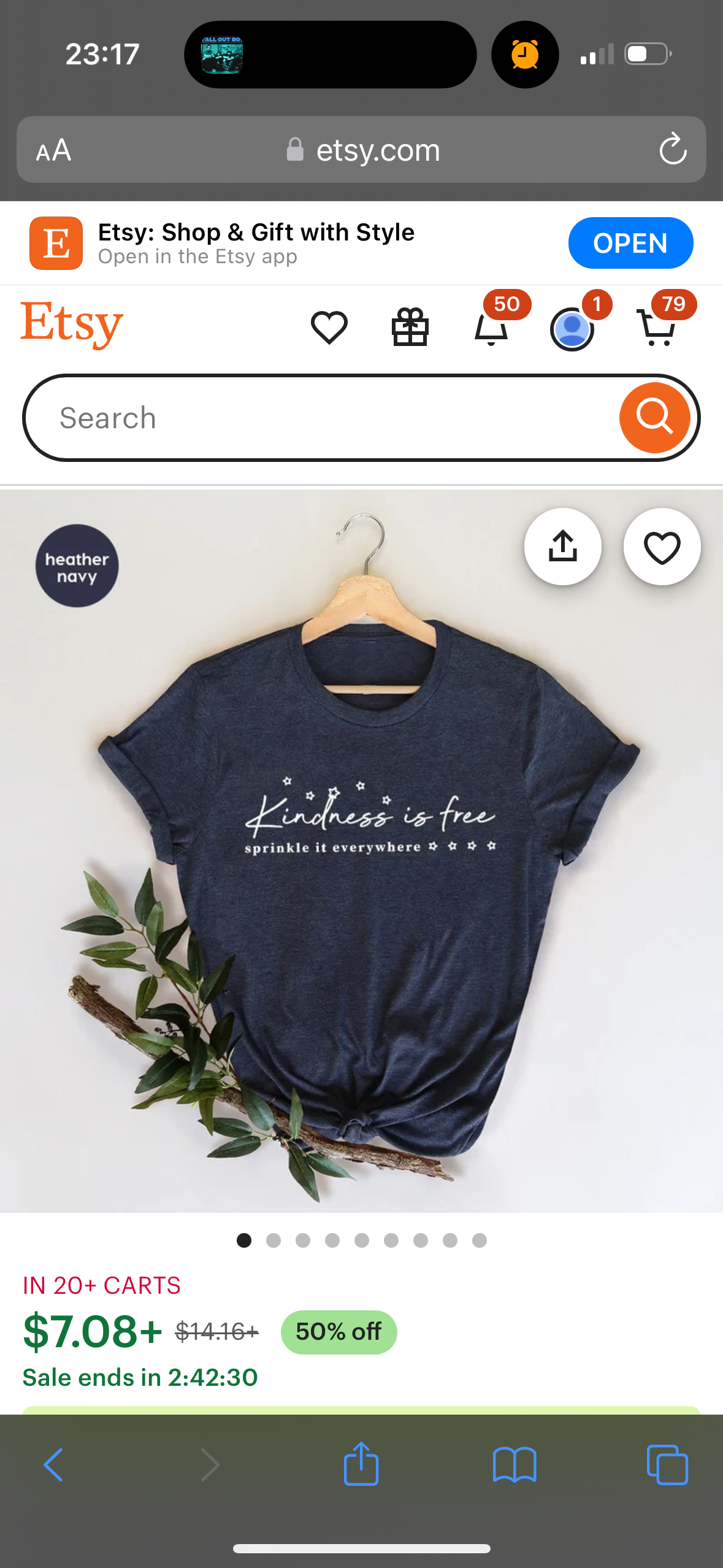 a mobile phone screen showing an etsy product listing for a heather navy tshirt that says "kindness is free, sprinkle it everywhere".  the price is $7.08, marked down from $14.16 with a 50% off sale.  the sale ends in 2:42:30.  the background is a white surface and a green plant.  the etsy logo is at the top of the screen.