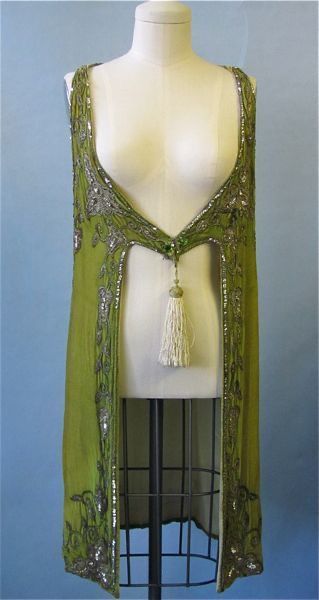 a mannequin wearing a sleeveless, green dress with beaded detailing and a tassel hanging from the front.