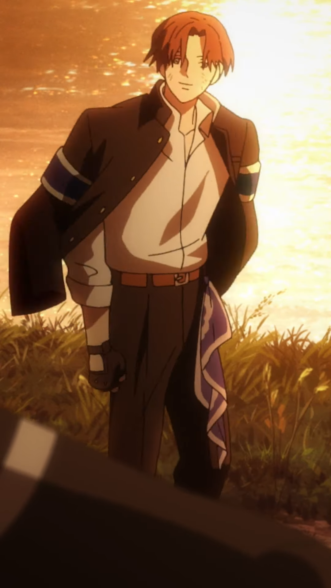 the image shows a young man with brown hair and brown eyes standing in a field of tall grass. the sun is setting behind him, creating a warm, golden light. he is wearing a dark blue jacket with a white shirt, dark pants, and a blue scarf around his right wrist. he is smiling slightly and looking off to the right of the frame.