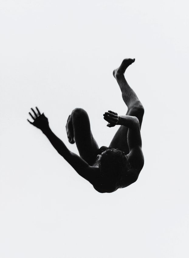 a black and white photograph of a male athlete in midair as he performs a jump, his body is completely silhouetted against a white background.  his limbs are extended in a graceful position, suggesting a sense of motion and athleticism. the image captures a moment of weightlessness and freedom, highlighting the beauty and power of human movement.
