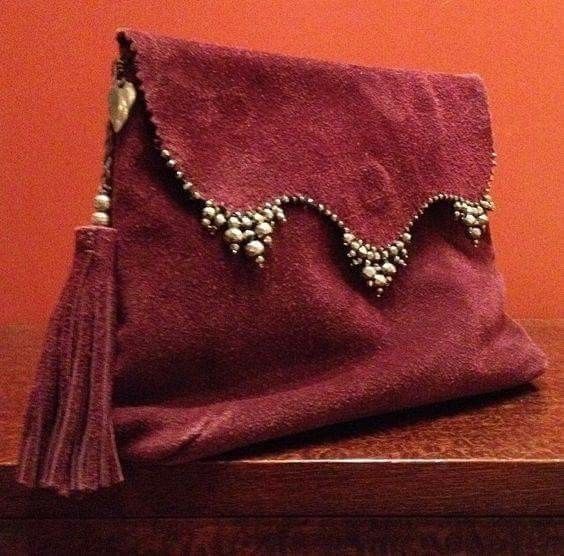 a maroon suede purse with a tassel is on a wooden surface. the purse has beaded detailing along its top edge. the background is a solid orange color.