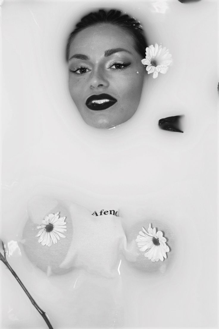 a black and white portrait of a woman in a milk bath. the woman has flowers in her hair and daisies around her. the image is minimal and  focused on the woman's face and body.