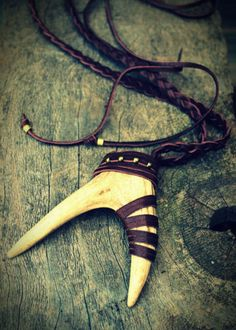 an overhead shot of a tribalstyle necklace featuring an animal tooth pendant wrapped with leather cords. the pendant and necklace rest on a weathered wooden surface. the necklace includes a braided cord and leather elements. the overall aesthetic is rustic and handmade.
