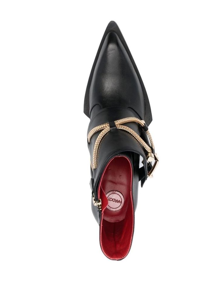 a topdown closeup shot of a single black leather haricot ankle boot with a pointed toe.  the boot features gold chain and buckle detailing around the ankle.  the inside of the boot is lined with red leather and a small haricot label is visible. the boot is presented against a plain white background.