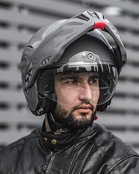 a man with a serious look on his face, wearing a grey motorcycle helmet with a black visor. he is also wearing a black leather jacket, looking straight ahead. the image highlights the helmet's design and the man's determined expression.  this could be a safetyfocused ad for motorcycle helmets.
