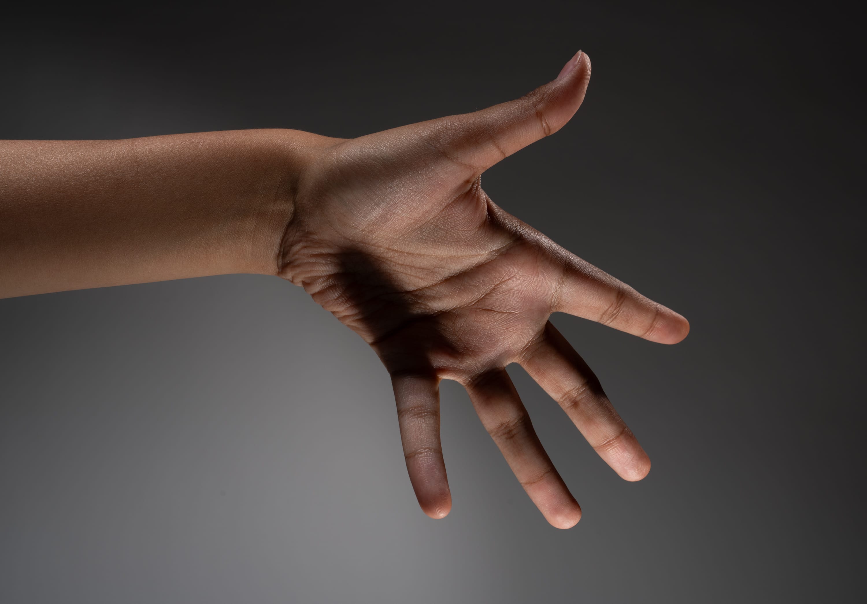 a closeup image of a person's hand reaching out with an open palm, suggesting a gesture of offering or asking for something. the hand is illuminated by studio lighting, casting subtle shadows that highlight the contours and texture of the skin.