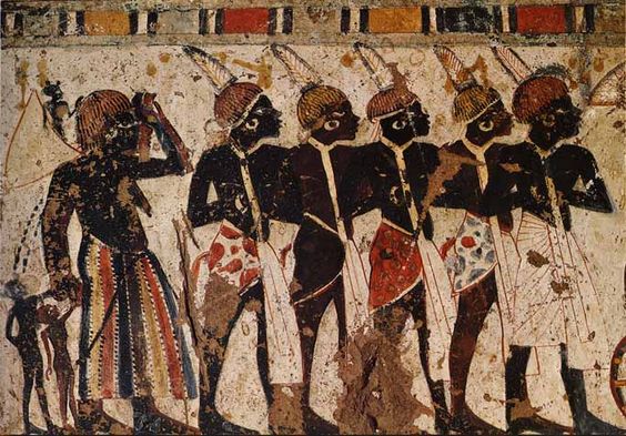 the image shows an ancient egyptian painting of a group of nubians. they are standing in profile and wearing white kilts with colorful sashes. they have dark skin and are wearing feathered headdresses. they are carrying bows and arrows.  the background of the painting is a light beige color. the painting is faded and cracked in some areas.