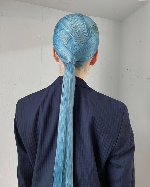 a woman with blue hair is wearing a dark blue jacket and has her hair pulled back in a ponytail.
